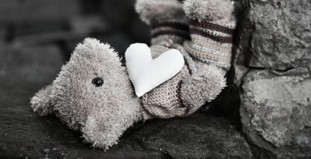 Ein Teddybär mit Herz kopfüber liegend auf einem Stein in schwarz-weißer Darstellung